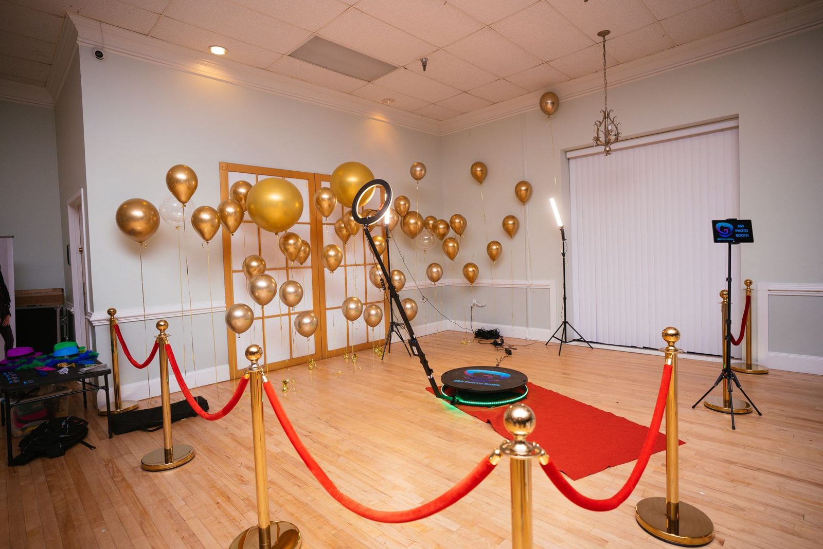 360 Photo Swirl platform with gold balloon backdrop and red carpet, ring light arm extended over the platform