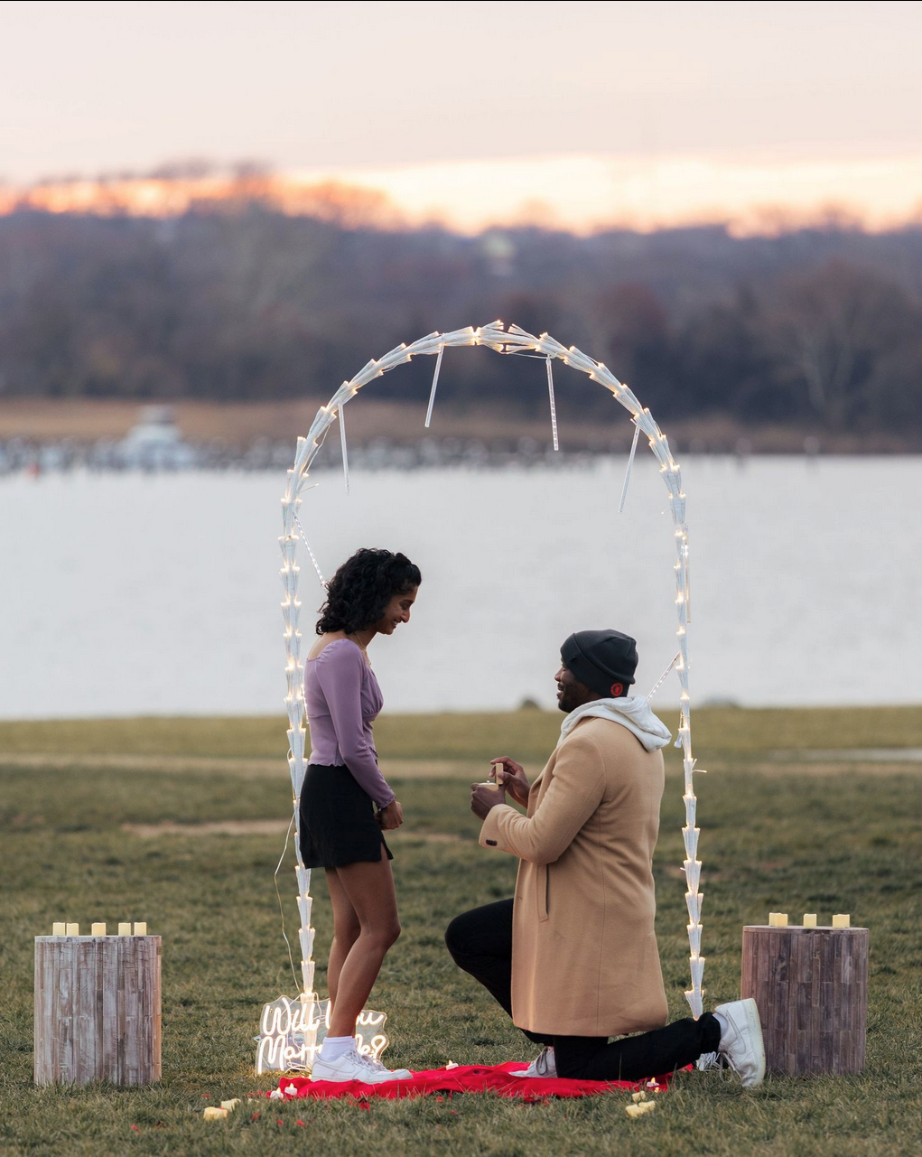 Proposal under a lit archway at sunset by the water