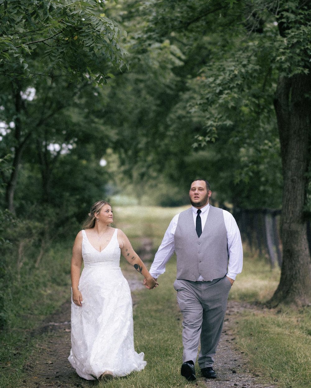 Bride and groom holding hands walking down a tree-lined path
