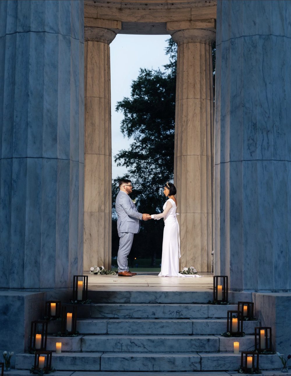 Couple holding hands between marble columns lit by candlelight