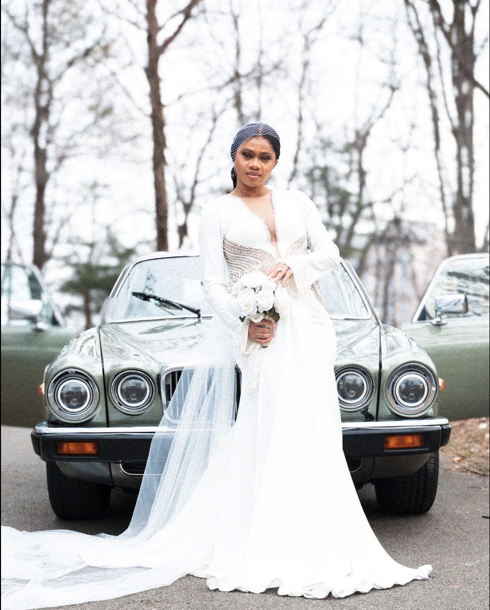 Bride posing in front of vintage cars with a birdcage veil